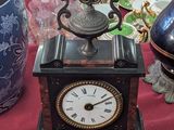 a small clock sitting on a table next to a vase