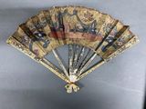 a fan with a design on it hanging on a wall