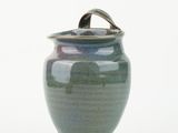 a green vase with a lid sitting on a white surface