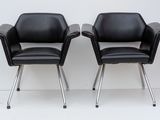 pair of black leather chairs with chrome legs against a white wall