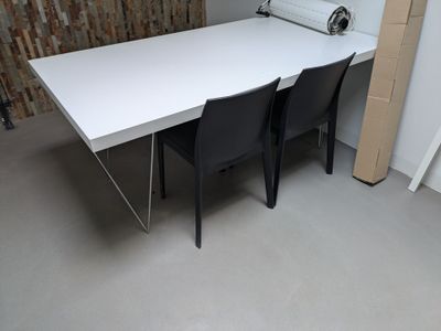 une table blanche avec deux chaises noires devant un mur de briques