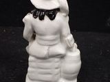 a white figurine of a woman with a hat and a bag