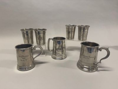 quatre tasses en métal argenté et quatre verres posés sur un plan de travail blanc