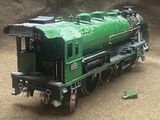 a green toy train sitting on the tracks in the dirt