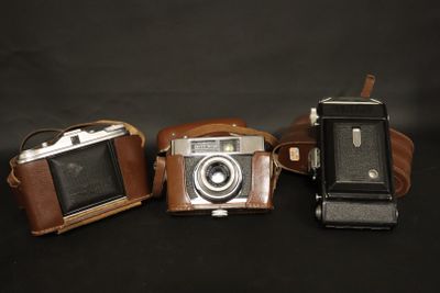 three old cameras sitting next to each other on a black background