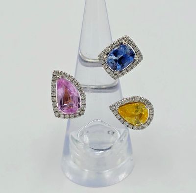 three different colored sapphire and diamond rings on a clear glass stand