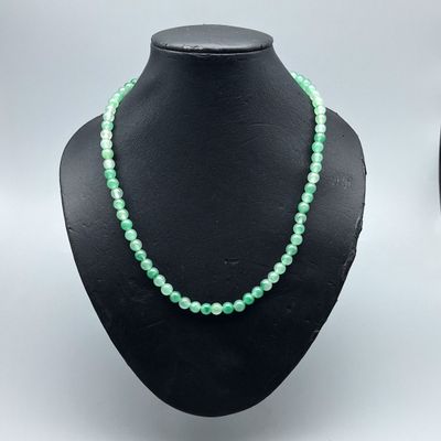 a close up of a necklace with green beads on a mannequin