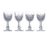 four crystal wine glasses are lined up on a white surface
