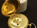 une petite montre de poche en or posée sur une surface noire