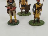 three figurines of knights with flags and shields on a white surface