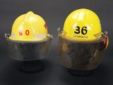 two yellow hard hats with face shields on a black background