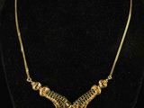 a gold necklace on a mannequin neck with a black background