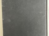 an old black book sitting on top of a table next to a white wall