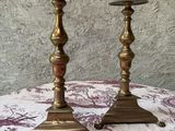 une paire de bougeoirs en laiton posés sur une table recouverte d'une nappe à motifs floraux violets et blancs