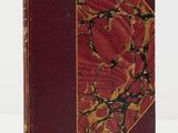 an old book with a red cover sitting on a white surface
