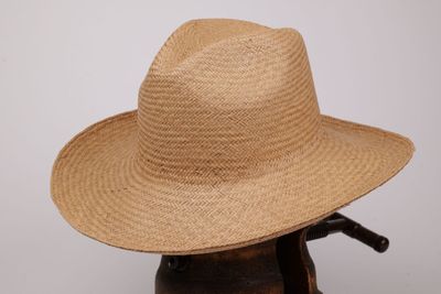 une image représentant un chapeau de paille posé sur un support en bois