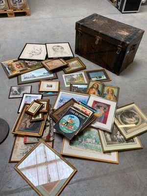a pile of framed pictures on the floor next to a trunk