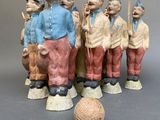 several figurines of men are standing next to a ball on a gray surface