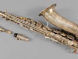 an old silver saxophone with a silver case and keys on a gray surface