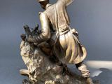 bronze statue of a man on a rock with a bird in his hand