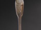 an antique silver plate with a spoon and fork on a table