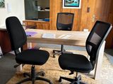two black office chairs sitting in front of a wooden desk