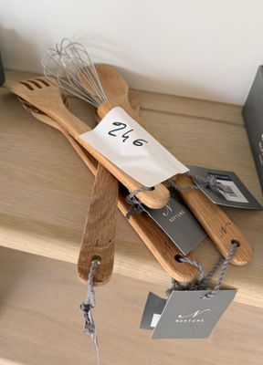 des ustensiles en bois posés sur une étagère, avec des étiquettes accrochées dessus