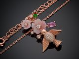 a close up of a necklace with a bird and flowers on it