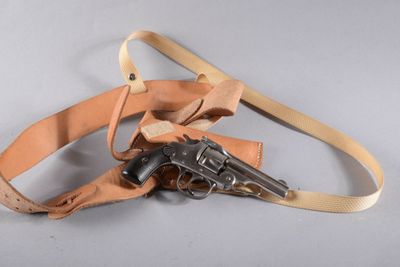 une ceinture à laquelle est fixée une arme, posée sur une surface blanche