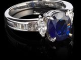 une photo d'une bague sertie d'un saphir bleu et de diamants, posée sur une surface noire