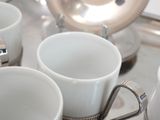 several white coffee cups are lined up on a silver tray