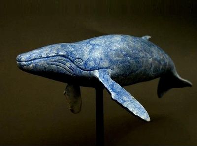 statue d'une baleine bleue posée sur un socle noir, devant un fond sombre