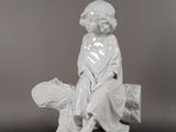une figurine blanche représentant un garçon assis sur un rocher avec un poisson
