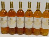 six bottles of wine are lined up in a row on a white surface