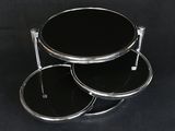 table en verre noir à trois niveaux avec des pieds chromés, sur fond noir