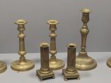 six brass candlesticks are lined up on a white surface