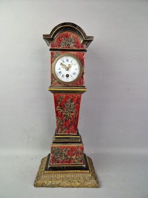 une horloge rouge et dorée posée sur une surface blanche