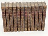 six old books are lined up in a row on a white surface