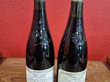 two bottles of wine sit on a table in front of a red wall
