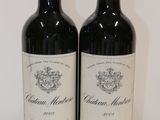two bottles of red wine sitting on top of a white table