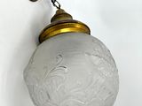 an old fashioned light fixture with a glass shade hanging from the wall