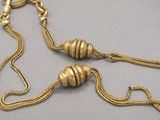 gold plated necklace with a chain and two beads on a gray surface