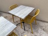 des chaises jaunes et une table sur une terrasse, près d'un mur
