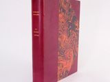 an old book with a red cover sitting on a white surface