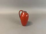 a small red vase with a handle on a table