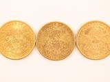 three gold coins are sitting side by side on a white surface
