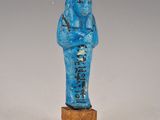 statue d'un homme vêtu d'une robe bleue, debout sur un bloc de bois