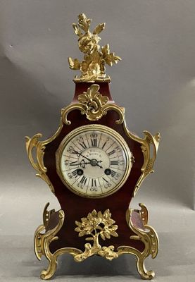 a red and gold clock sitting on a white surface