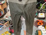 a man standing in a garage holding a pair of waders