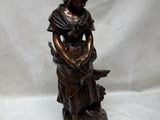 statue en bronze représentant une femme assise sur un rocher avec un chien